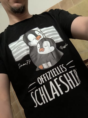 Kunde trägt das personalisierte schwarze Schlafshirt mit einem Motiv von zwei schlafenden Pinguinen.