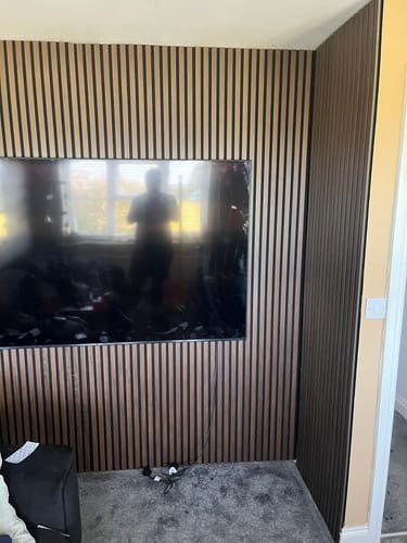 Customer's living room corner with light-colored Premium Acoustic Slatted Wall Panels installed as a feature wall behind a TV.