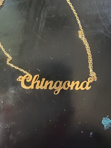 Customer's gold OG Chingona Necklace lying on a dark surface, showing the nameplate clearly.