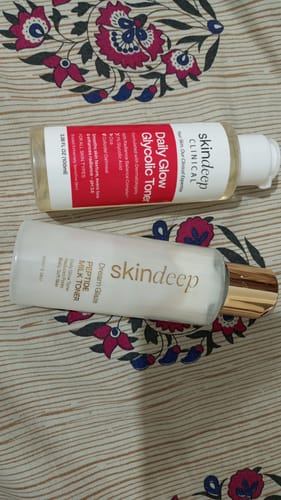 Reviewer's Daily Glow Glycolic Toner bottle shown with another skincare product on a patterned surface.
