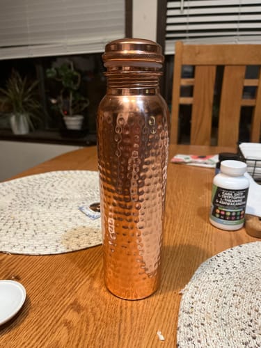 Reviewer's hand-hammered copper water bottle sitting on a wooden dining table.