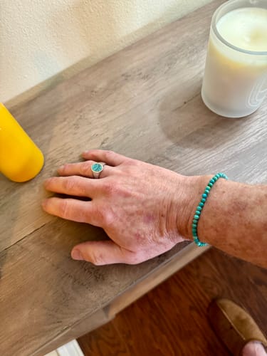 Customer wearing the Turquoise Bead Bracelet on their wrist while resting their hand on a wooden surface.