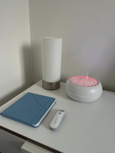 Reviewer's witte Sakura Aroma Diffuser op een nachtkastje. De bovenkant is rood verlicht en verspreidt een fijne nevel.