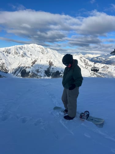 Reviewer standing on a snowy mountain wearing the baggy, light-colored waterproof snow pants.