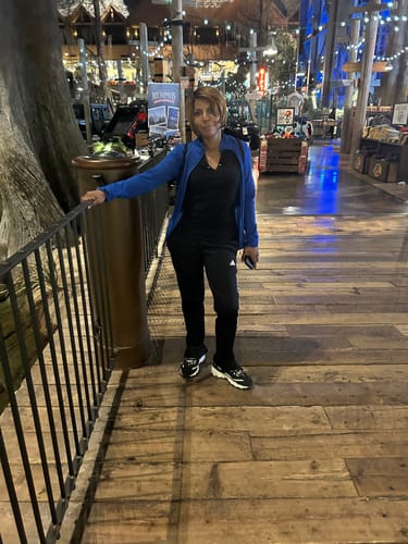 Reviewer standing on an indoor wooden walkway, wearing the Q CARLA full wig in a short, highlighted style.