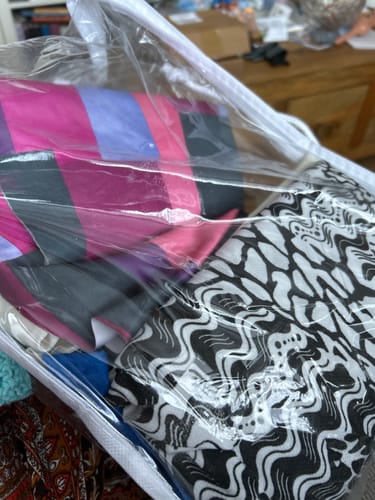 Customer's clear bag of Mixed Remnants Fabric, showing folded pieces with colorful striped and abstract patterns.