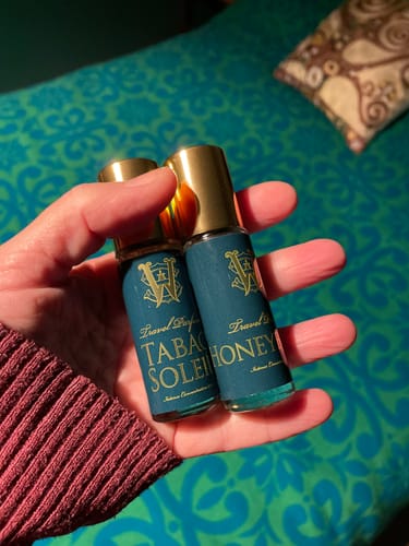 Reviewer holding the Honeyberry and Tabac Soleil travel-sized perfume bottles in their hand.