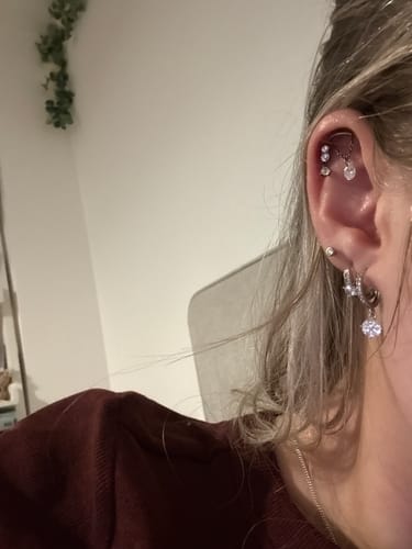 A close-up of a reviewer's ear showing the silver Dangle flatback stud with a crystal charm in a cartilage piercing.
