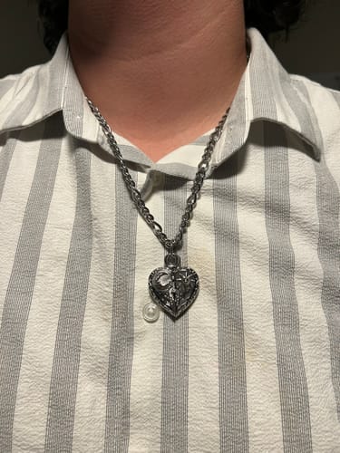 Close-up of a customer wearing the silver-colored COSMIC HEART PENDANT on a chain against a striped shirt.