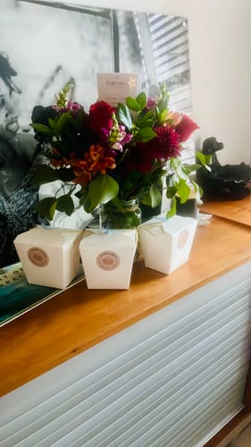 Customer's Charming Flower Arrangement with colorful red and orange blooms in a glass vase, displayed on a wooden sideboard.