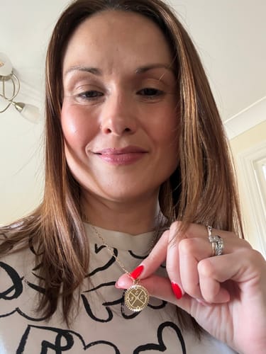Reviewer holding up the round, gold pendant of her Engravable Compass Necklace against her chest.