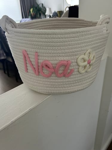 Customer's personalized knitted basket in white, with the name 'Noa' in pink yarn and a flower icon.