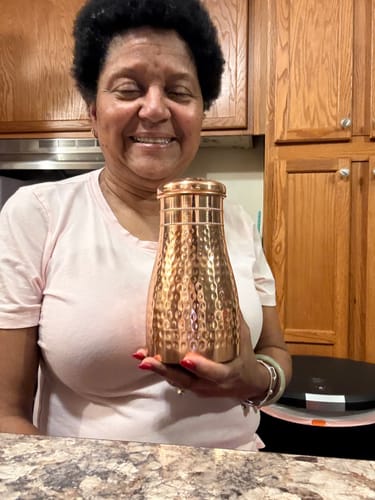 Customer smiling and holding the hammered copper Himalayan Ayurvedic Bedside Carafe in a kitchen.