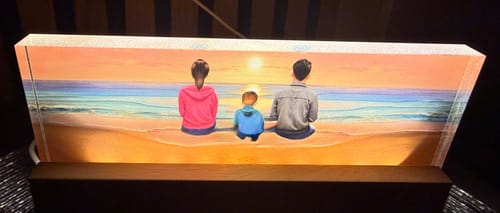 Rezensent zeigt den beleuchteten LED-Aufsteller mit einer dreiköpfigen Familie am Strand bei Sonnenuntergang.