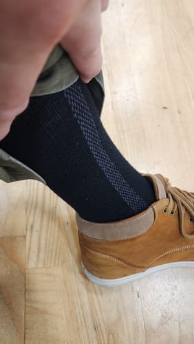Reviewer pulls up a pant leg to show the patterned detail on the black Men's Alpaca Socks.