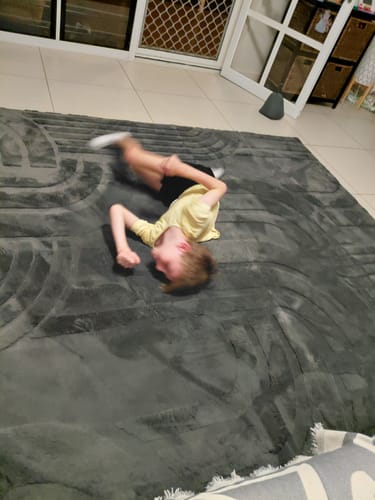A customer's child playfully rolling on the large, charcoal Mellow Mat in a living room.