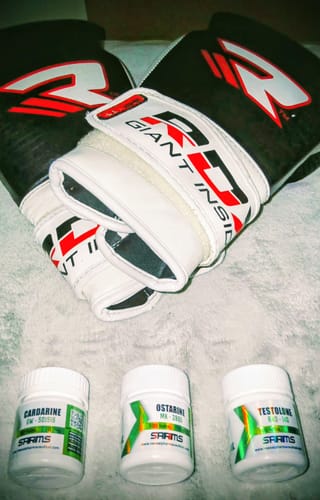 El cliente muestra los tres botes del combo de masa muscular magra y fuerza, junto a unos guantes de boxeo.