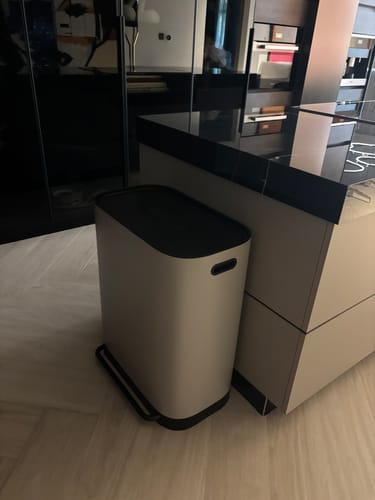 Customer's light-colored dual compartment recycle bin with a black lid, shown in a modern kitchen.