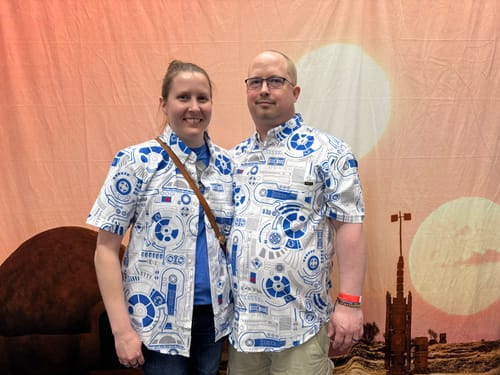 Two customers wearing matching Star Wars™ 'R2 Deconstructed' shirts against a themed backdrop.