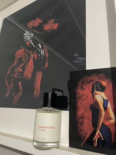 Customer's Magnum Opus perfume bottle on a white shelf, displayed with two pieces of dark artwork.