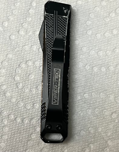 Reviewer shows the back of the VT Mini Stinger OTF Knife with its pocket clip and chipped black paint.