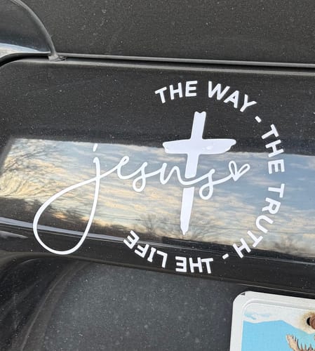 Reviewer's white Jesus window sticker with a cross and script, applied to the body of a black car.