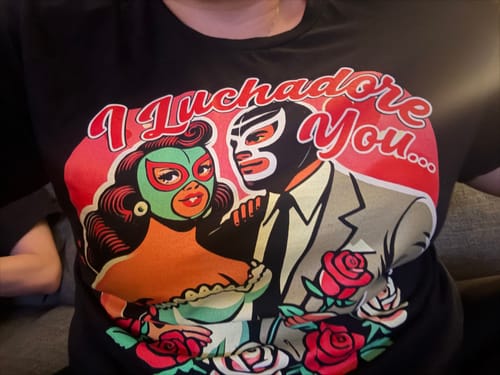 Close-up of a reviewer wearing the 'I Luchadore You' T-shirt, showing the vibrant luchador graphic.
