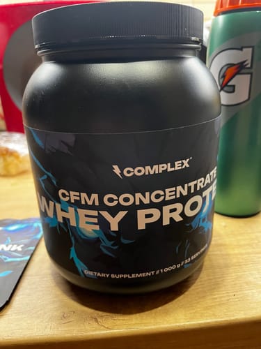 Customer's black tub of Complex CFM Whey Protein sitting on a wooden table.