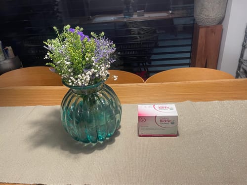 Rezensent zeigt die OMNi-BiOTiC HETOX INT Packung auf einem Tisch neben einer Blumenvase.