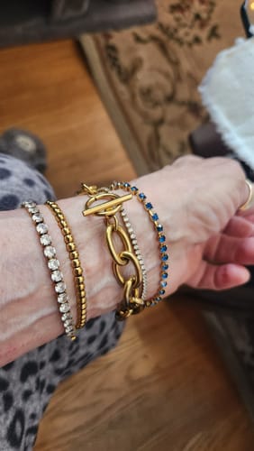 Reviewer's wrist showing a stack of four bracelets, including two Fae Tennis Bracelets with clear and blue stones.