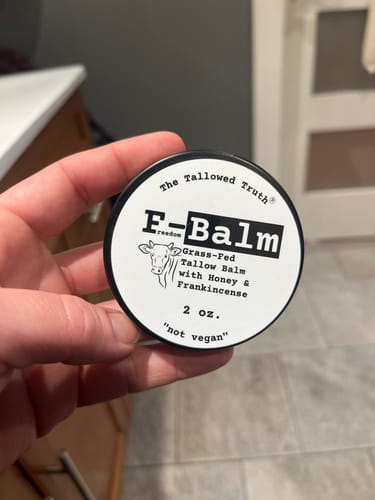 Customer holding the round, black tin of F-Balm tallow balm, showing the label.