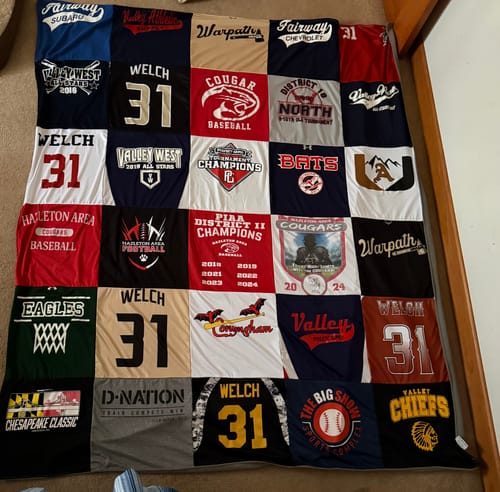 Customer's finished Premium T Shirt Quilt made from numerous sports jerseys, laid out on the floor.