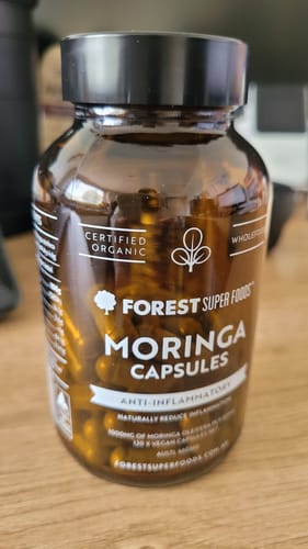 A customer's brown bottle of Organic Moringa Capsules from Forest Super Foods sitting on a wooden table.
