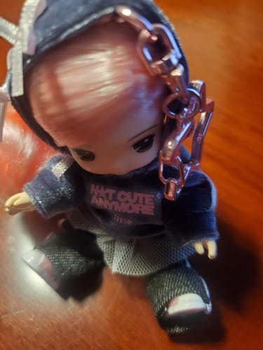 Customer's Little Mimi keyring doll from the ILLIT album, wearing a dark hoodie that says 'NOT CUTE ANYMORE'.