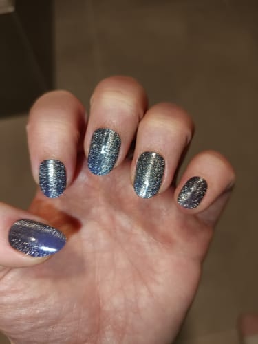 Hand einer Kundin, die die glitzernden „Midnight Cateye“ UV-Gelfolien mit Cateye-Effekt auf kurzen, abgerundeten Nägeln trägt.