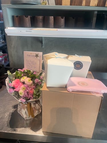 Customer's Blossom Beauty Posy, a fresh bouquet with pink and purple flowers, sits on a counter next to gift boxes.