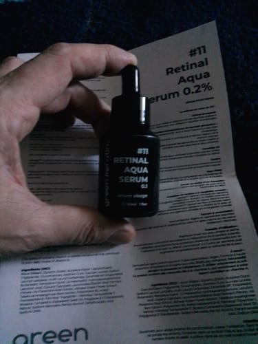 Un client tenant le flacon noir du Sérum Aqua au Rétinal #11 devant la notice du produit.