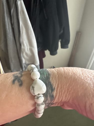 Close-up of a reviewer's wrist, showing a white Howlite crystal bracelet with a heart-shaped bead.