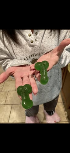 Reviewer holding two large, green D's-shaped gummy candies in their hands.