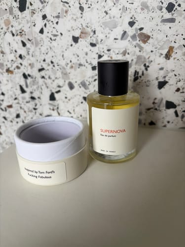 Reviewer's Supernova perfume bottle and its open packaging on a terrazzo-style surface.