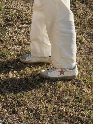 Customer wearing PAULA MINI sneakers with a pink glitter star and beige suede toe cap on a grassy area.