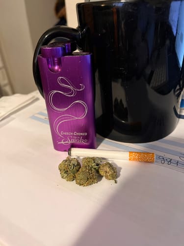 Customer's Purple Punch buds next to a purple one-hitter pipe and a black mug on a table.