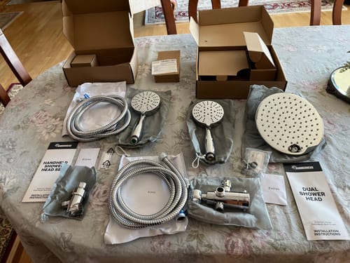 Customer displays the unboxed 3-Spray Dual Shower Head kit with its shiny metal components on a table.