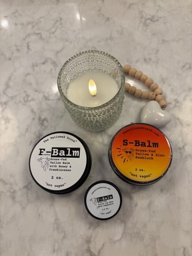 Customer's F-Balm and S-Balm skincare tins displayed on a marble countertop next to a candle.