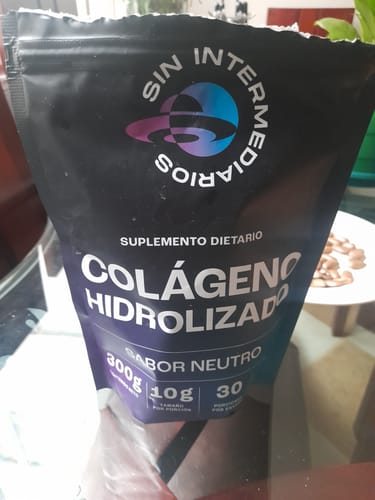 Una persona sosteniendo la bolsa negra del suplemento Colágeno Hidrolizado en un interior.