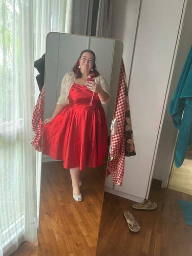 Reviewer taking a mirror selfie in the shiny red Jawbreaker Swing Dress, holding out the full skirt.