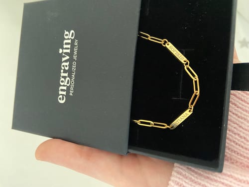 Customer holds open a jewelry box showing the gold Aurora necklace with an engraved link chain.