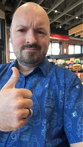 Reviewer gives a thumbs-up while wearing the blue Mega Man "Megamatics X" short sleeve shirt with its schematic pattern.