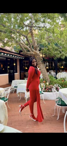 Customer posing outdoors in a red Naked Closed Toe Jumpsuit, styled with a matching skirt.