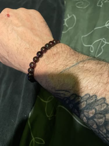 Client montrant son Bracelet Grenat aux perles sombres porté à son poignet.